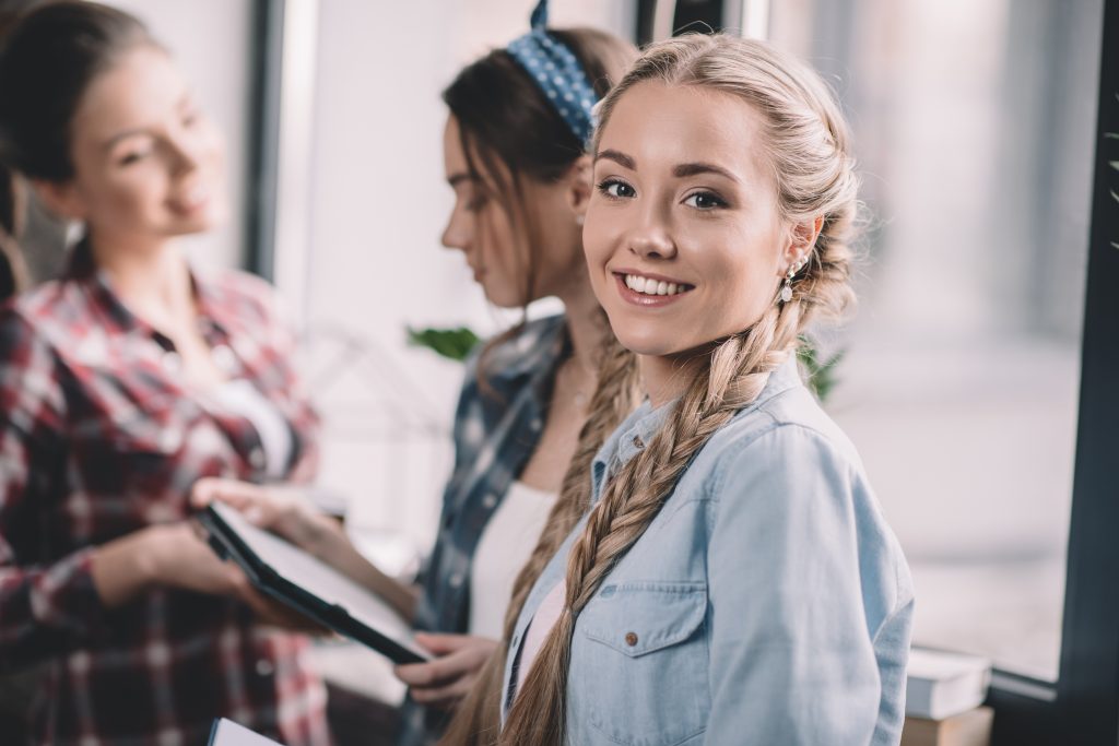 Beautiful girl student smiling while standing near colleagues
